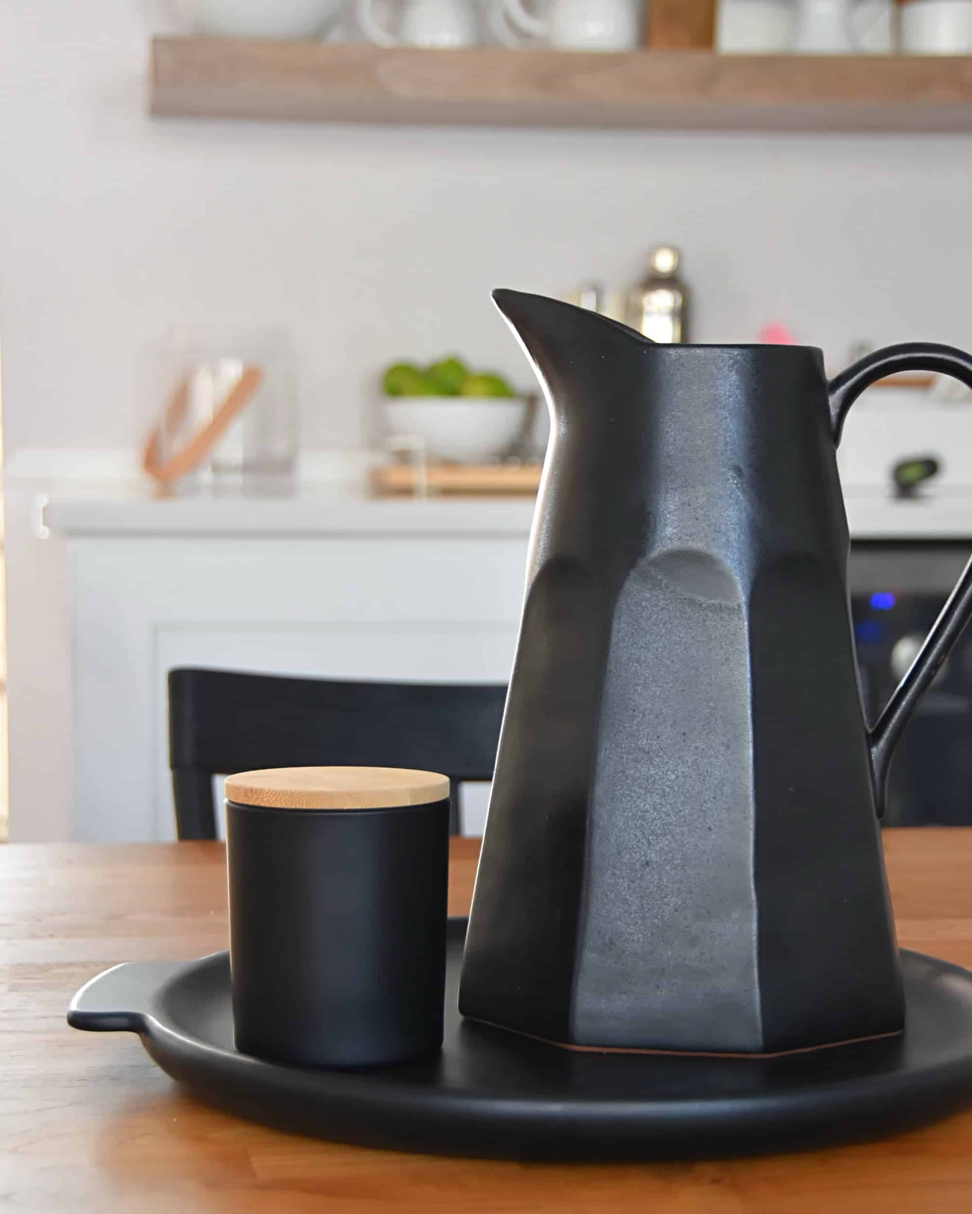 A platter on a dining room table with a large black vase and a Rowe Casa Organics candle side by side.