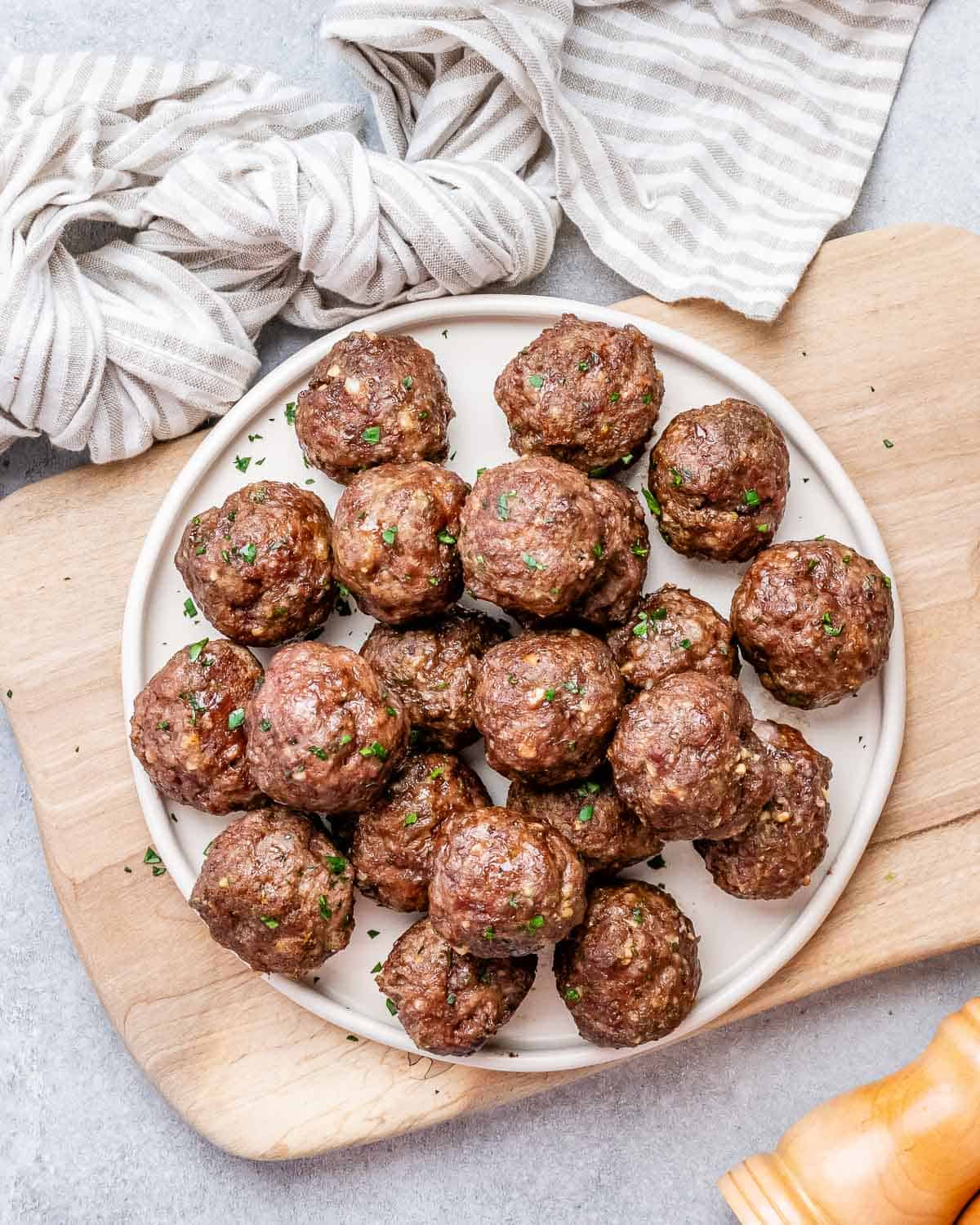 A white round plate filled with meatballs on a cutting board.