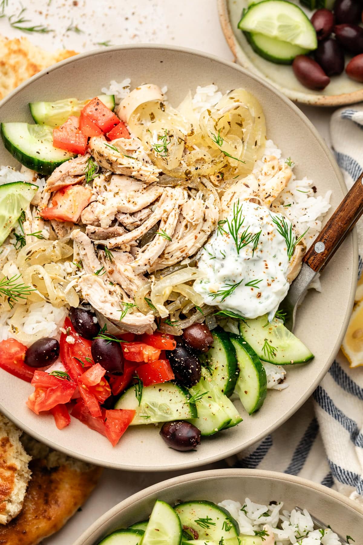 A plate with chicken, cucumbers, olives, tomatoes, rice, and Tzatziki sauce.