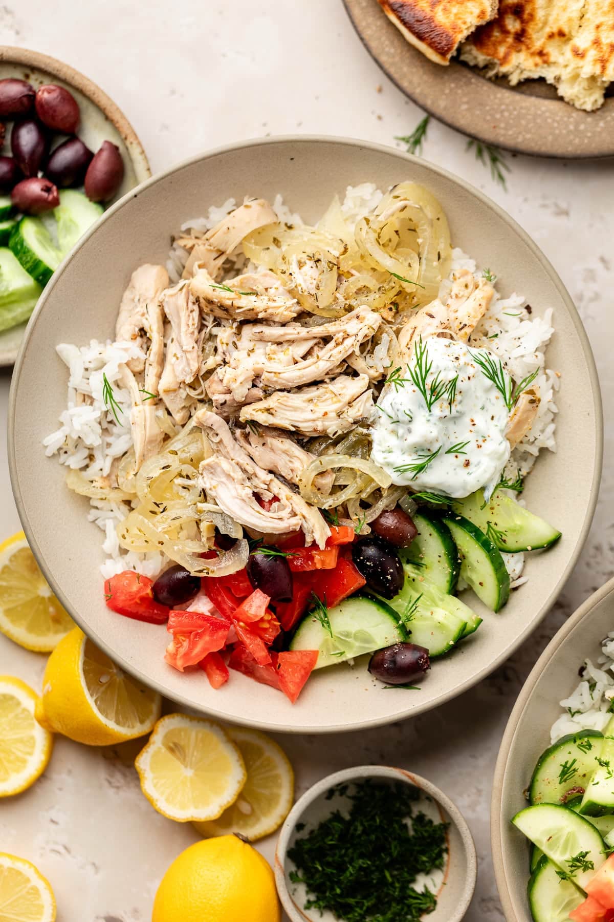 A plate with rice, a Greek salad, and slow cooker Greek chicken on top with Tzatziki and fresh herbs.